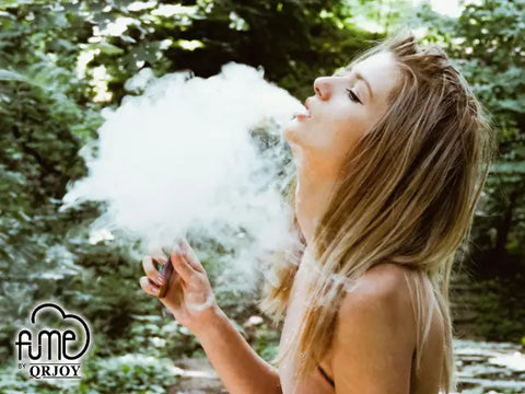 A woman with long blonde hair exhales a thick cloud from a handheld nicotine-free vaping device.