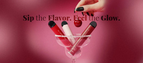 Three red and white disposable vape pens are arranged in a martini glass with sugar rim, alongside a single cherry.